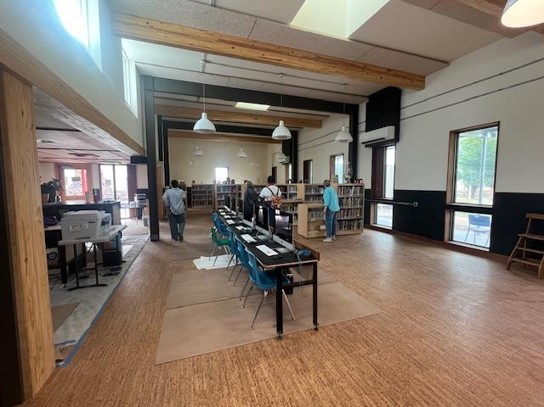 large open space room with wooden floors; row of narrow computer tables in the center with Mac computers on top; bookshelves and people browsing through the books