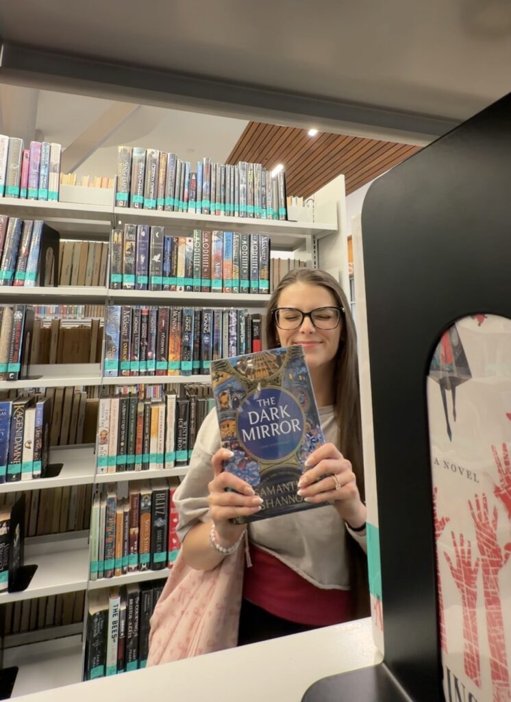 Alexzandra poses with the book Dark Mirror in a Dallas-Fort Worth Area Public Library