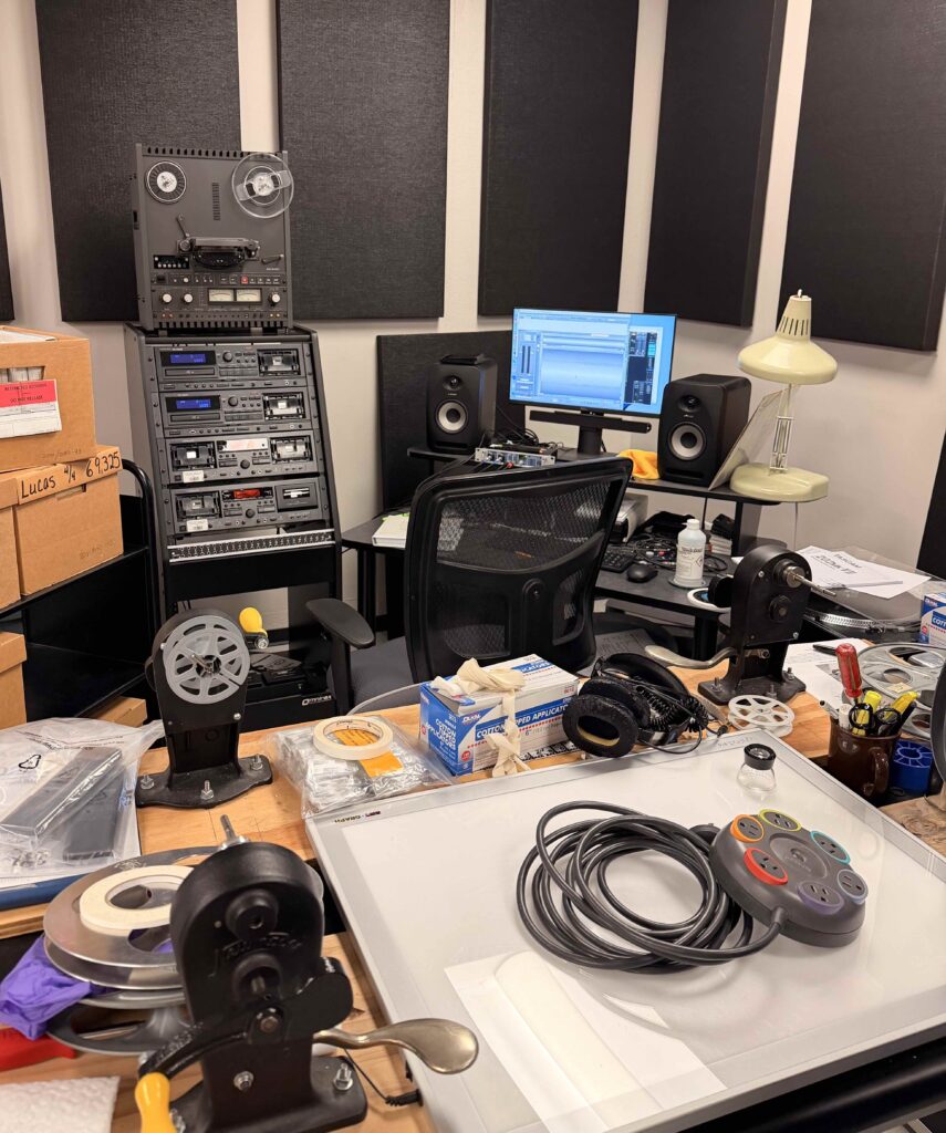 A desk is full of gear used to transfer old audio and video to digital with several machines in the background