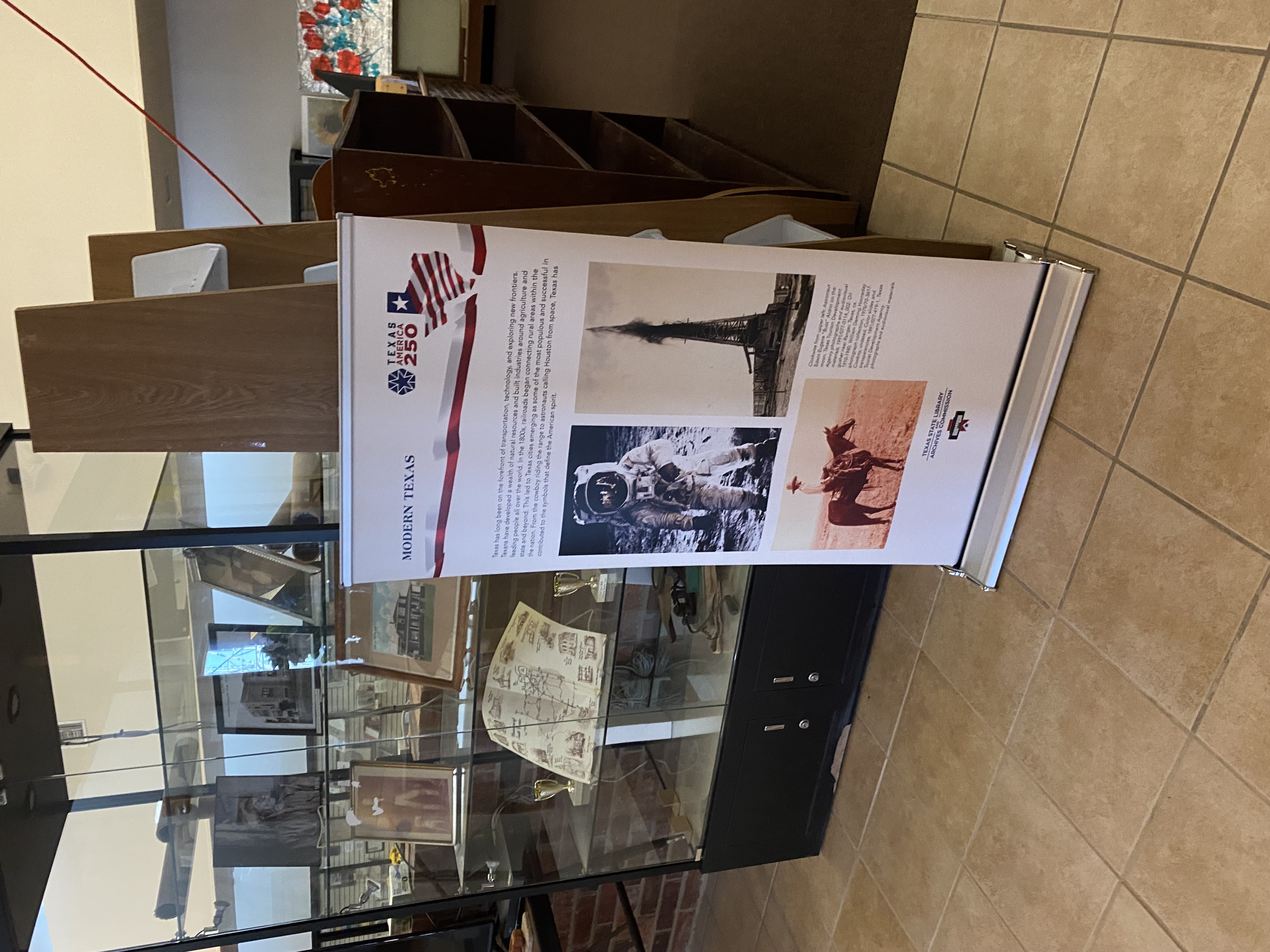 A Modern Texas Texas America250 banner next to a glass display case with framed photos and artifacts